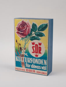 Rektangulär insamlingsbössa i trä, målad i blått med en tryckt etikett på framsidan.